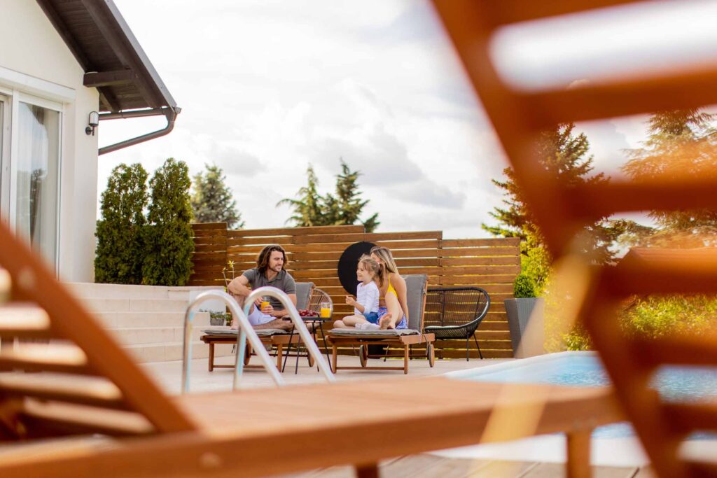 Young Family Relaxing By The Swimming Pool In The House Backyard